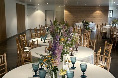 Salle de réception décorée avec des tables alignées, nappes blanches, chaises en bois et centre de table floral.