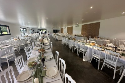 Salle de réception décorée avec des tables alignées, nappes blanches, chaises en bois et centre de table floral.