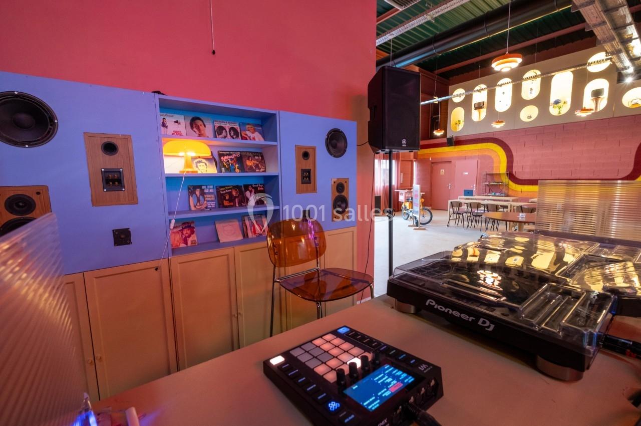 Salle colorée avec platine DJ, étagère de vinyles, haut-parleurs intégrés et mobilier rétro.