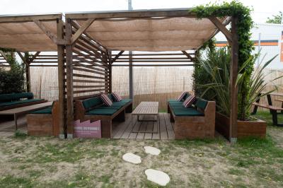 Salle lumineuse avec murs rouges, tables hautes en bois et métal, tabourets, affiches décoratives et luminaires modernes.