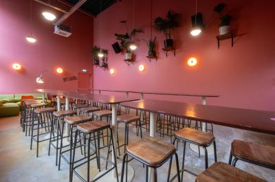 Salle lumineuse avec murs rouges, tables hautes en bois et métal, tabourets, affiches décoratives et luminaires modernes.