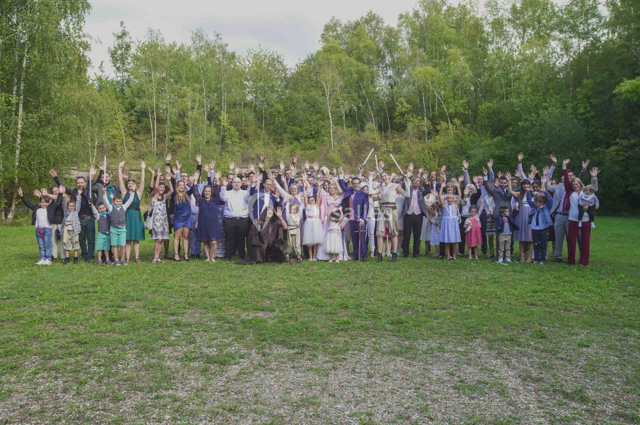Un grand groupe de personnes debout sur une pelouse, levant les bras, avec des arbres en arrière-plan.
