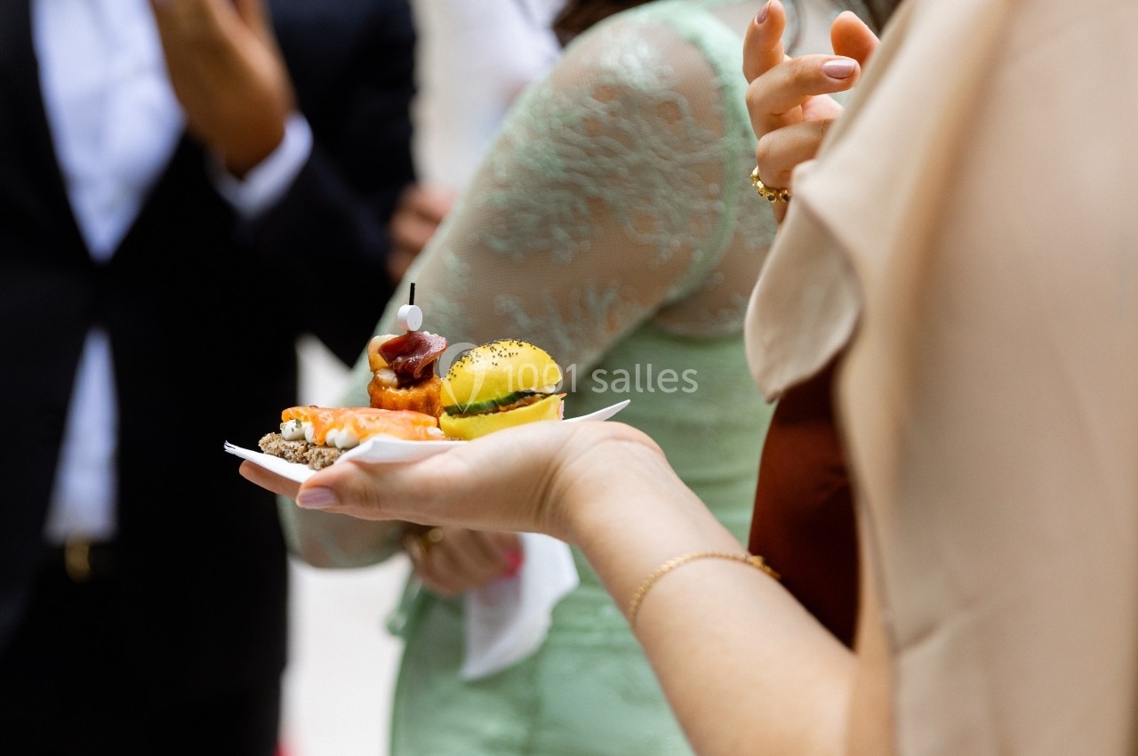Une main tenant une assiette avec des amuse-bouches variés lors d'un événement habillé.