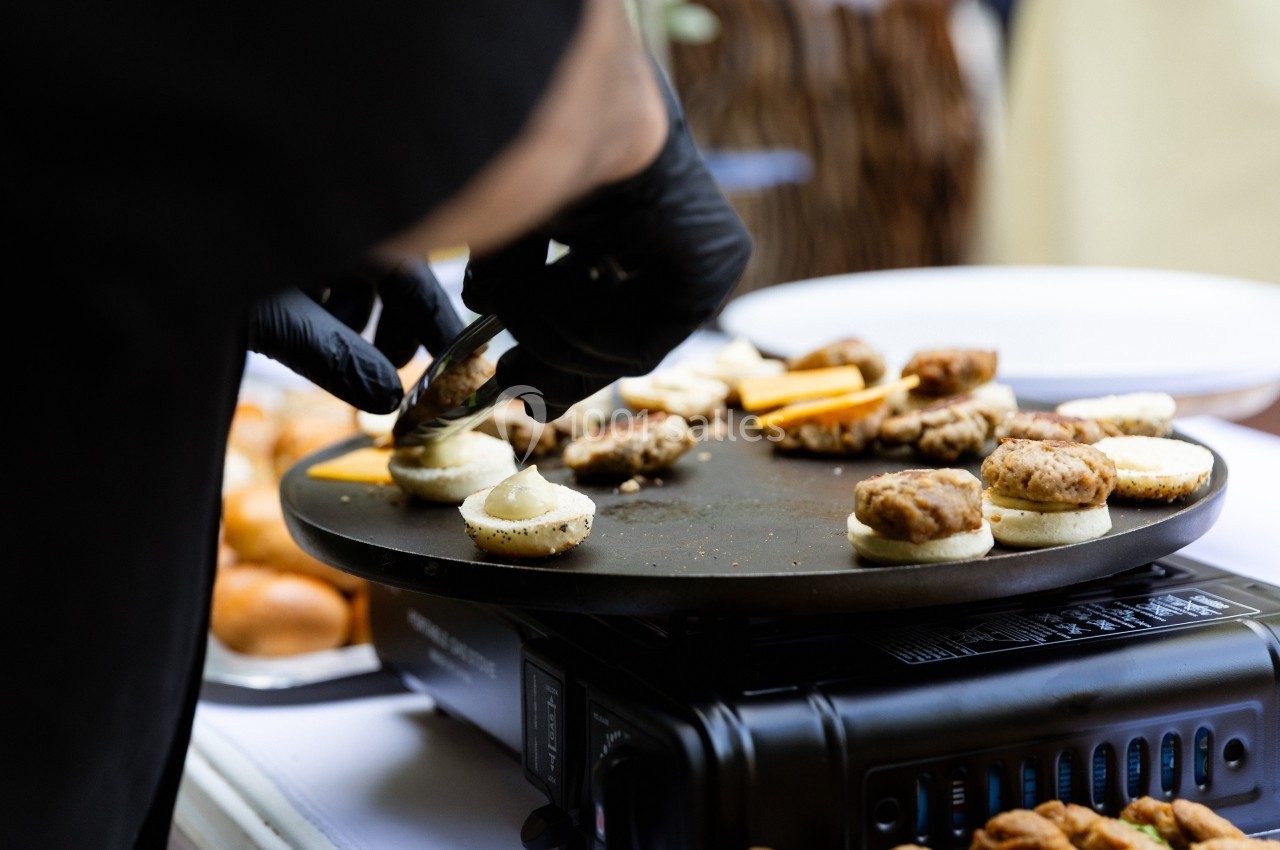Un cuisinier en gants noirs prépare des amuse-bouches sur une plaque chauffante lors d'un événement.