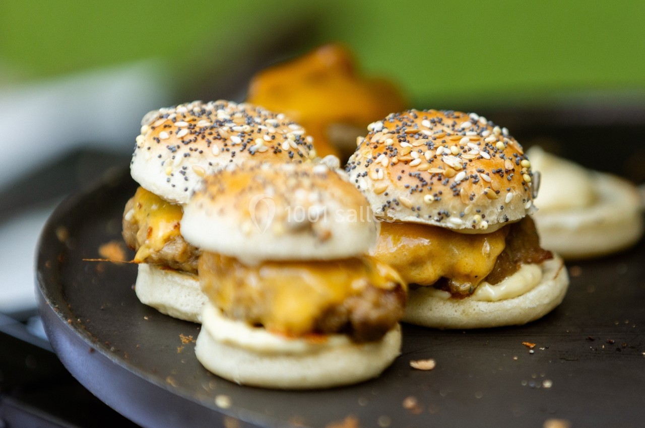Trois mini-burgers au fromage fondant sur une plaque de cuisson, avec des pains garnis de graines.