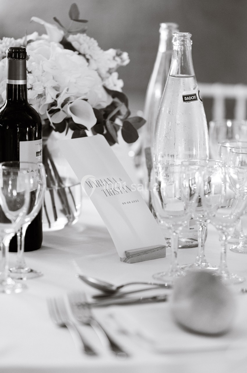 Table de réception élégamment dressée avec fleurs, bouteilles, verres et un menu portant des prénoms et une date.