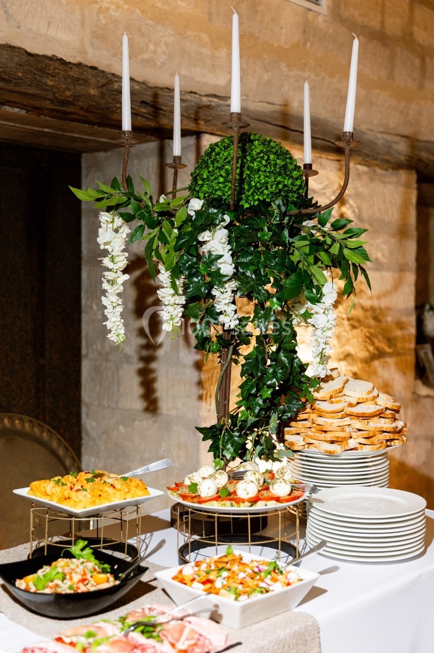 Buffet décoré avec des bougies, des plantes et des plats variés, comprenant tartes, salades et assiettes de pain empilé.