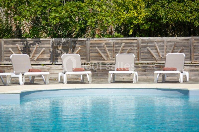 Chaises longues alignées près d'une piscine, avec des serviettes pliées, entourées de verdure et d'une clôture en bois.