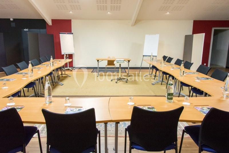 Salle de réunion aménagée en U avec tables, chaises, paperboards, bouteilles d'eau et un vidéoprojecteur.