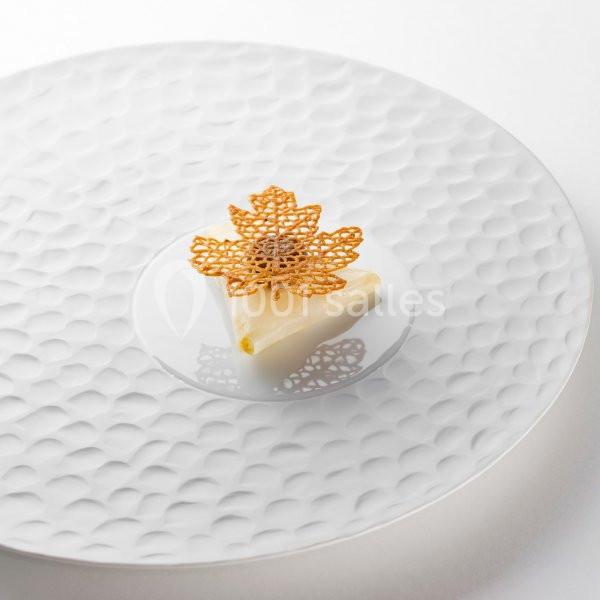 Une assiette blanche contenant un dessert raffiné avec une décoration en dentelle comestible en forme de feuille.