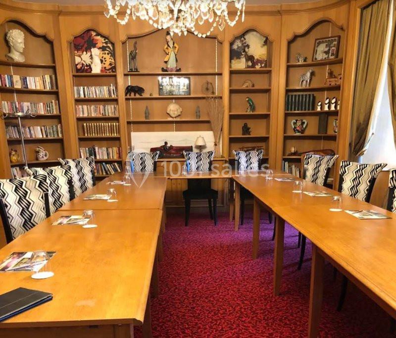 Salle de réunion avec tables en bois disposées en U, chaises à motifs et étagères décoratives en arrière-plan.