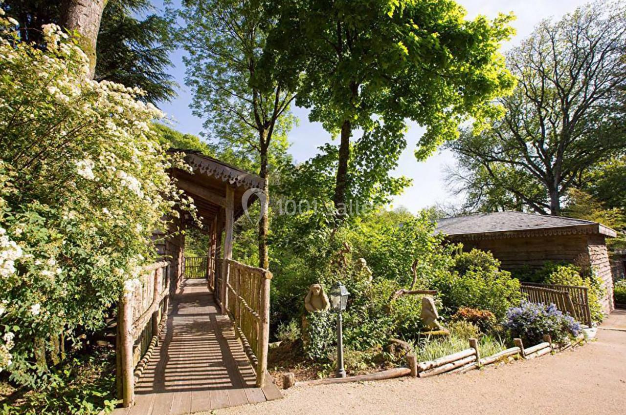 Passerelle en bois entourée de végétation luxuriante et reliant deux bâtiments dans un cadre naturel.