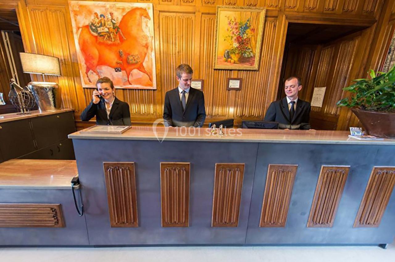 Trois réceptionnistes en uniforme travaillent derrière un comptoir dans un hall décoré de peintures colorées.