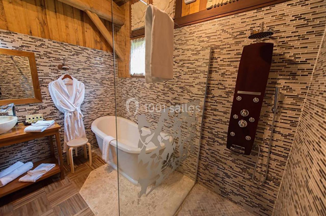 Salle de bain avec baignoire, douche à l'italienne, peignoirs suspendus et murs en mosaïque beige et marron.