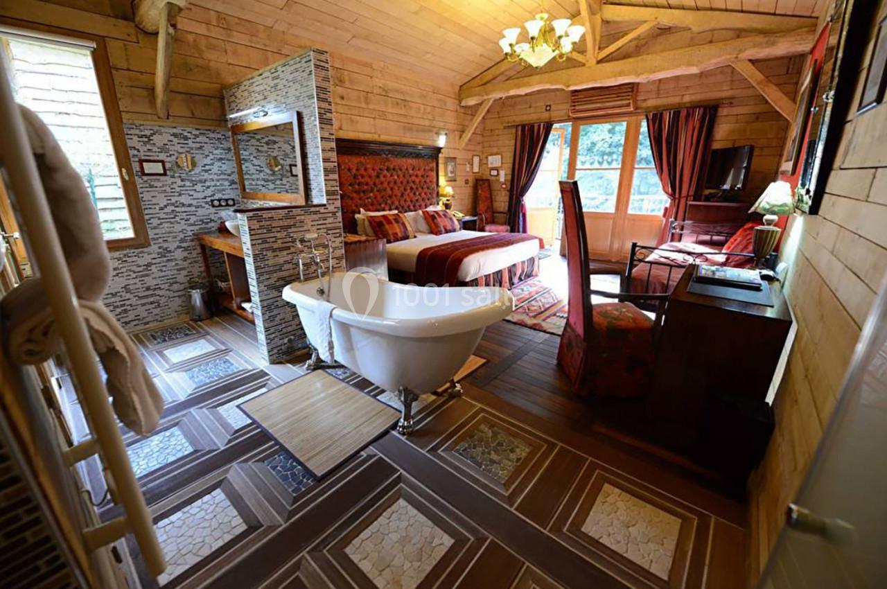 Chambre en bois avec baignoire sur pied, lit double, bureau, fauteuils et grande fenêtre donnant sur l'extérieur.