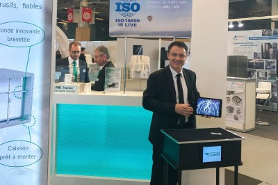 Un homme en costume tenant une tablette affichant des applications, avec un smartphone placé devant l'écran.