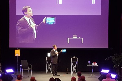 Un homme en costume tenant une tablette affichant des applications, avec un smartphone placé devant l'écran.