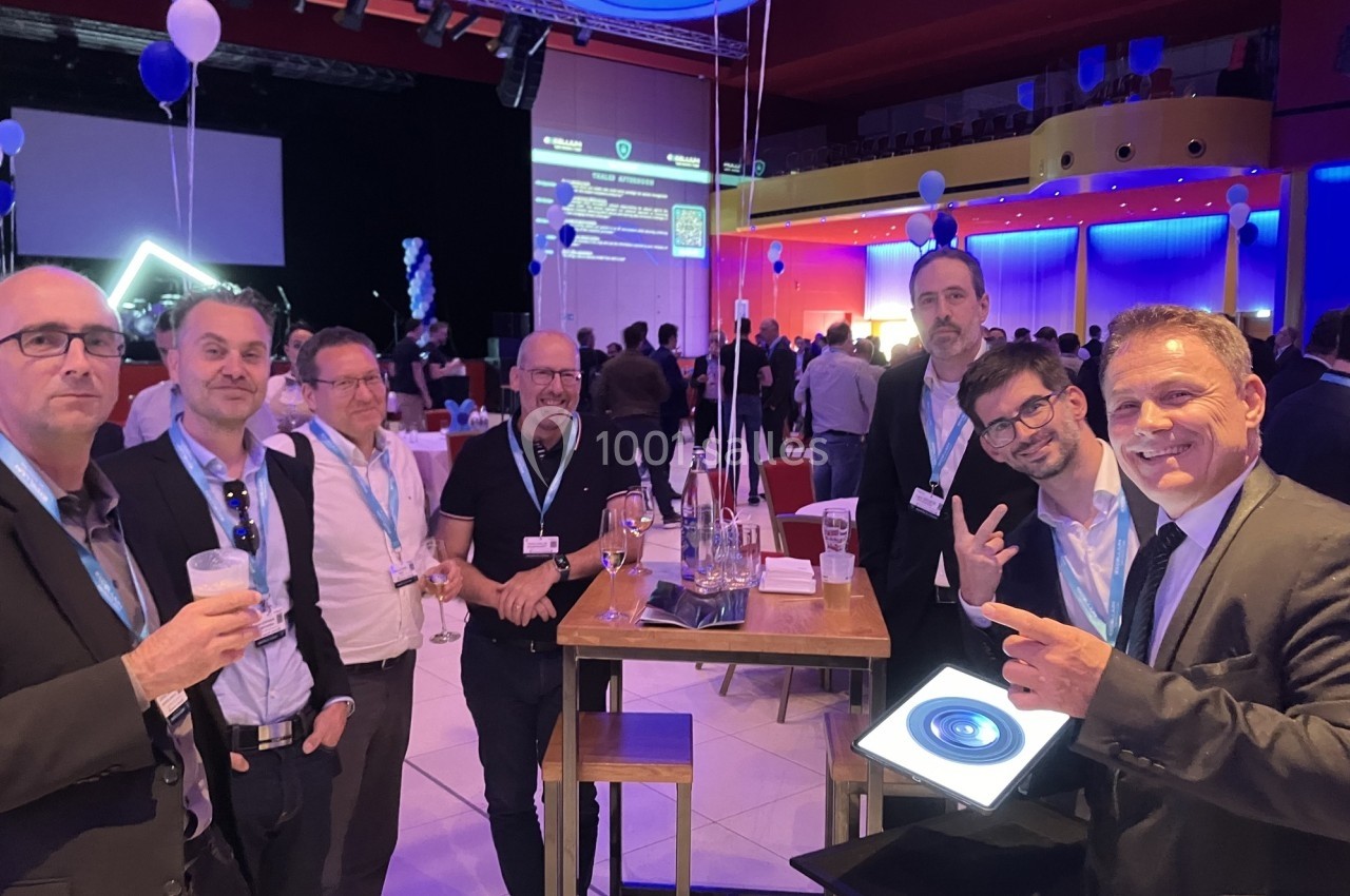 Groupe d'hommes en tenue professionnelle discutant autour de tables hautes lors d'un événement en intérieur.