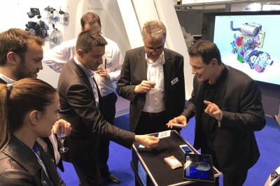 Un homme en costume tenant une tablette affichant des applications, avec un smartphone placé devant l'écran.