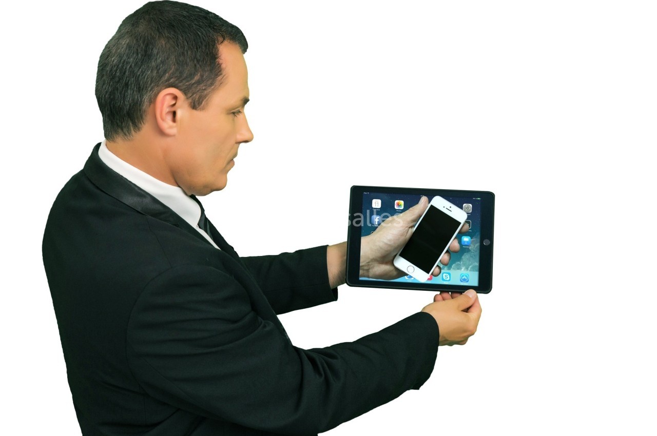 Un homme en costume tenant une tablette affichant des applications, avec un smartphone placé devant l'écran.