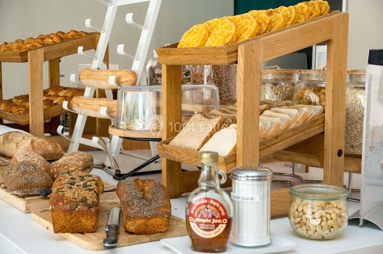 Buffet de petit-déjeuner avec pains variés, céréales, gaufres, noix et condiments sur une table.