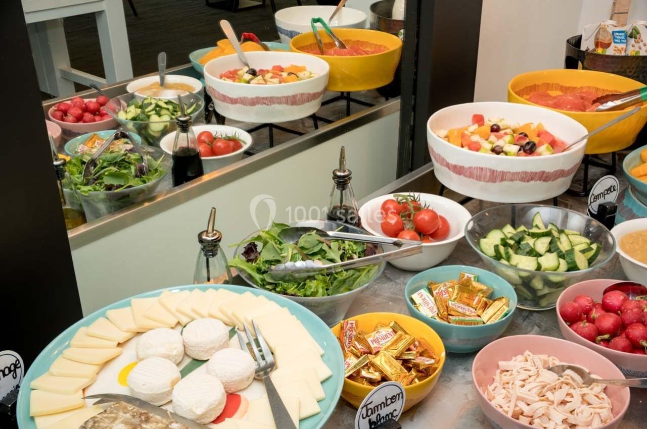 Buffet avec salades, légumes frais, fromages, charcuterie et condiments disposés dans des bols colorés.