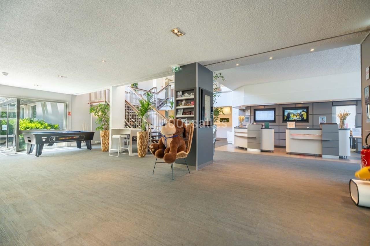 Hall d'accueil spacieux avec fauteuil, peluche, baby-foot, escalier et comptoirs d'information en arrière-plan.