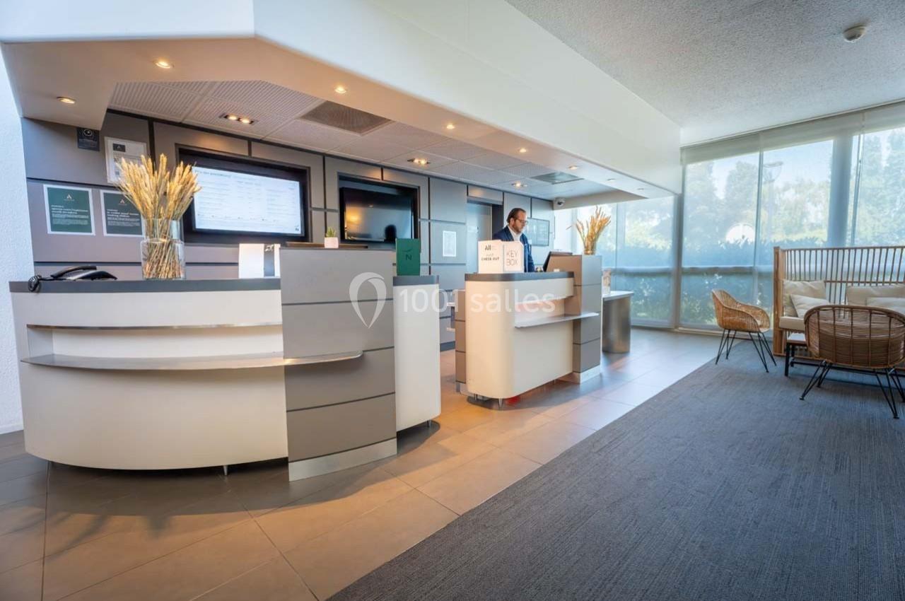 Accueil d'un hôtel avec un comptoir moderne, un employé en uniforme et un espace d'attente avec fauteuils en arrière-plan.