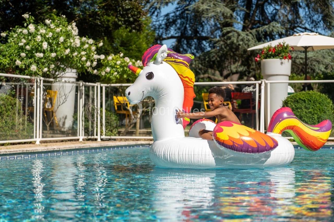 Un enfant souriant sur une bouée licorne colorée flottant dans une piscine en extérieur par une journée ensoleillée.
