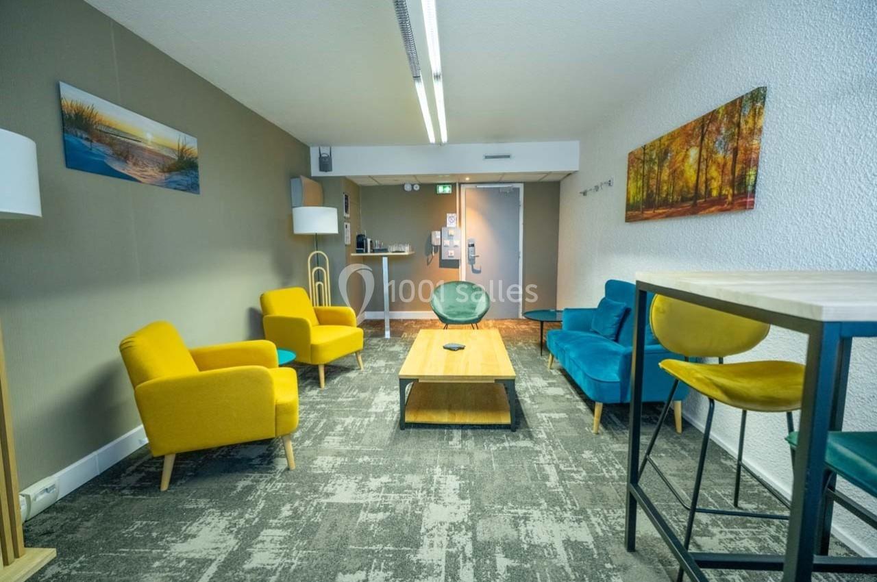 Salle de détente avec fauteuils colorés, table basse en bois, tapis gris et décorations murales.