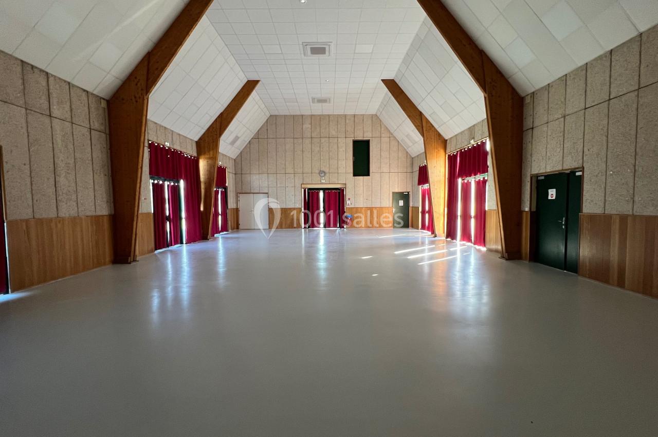 Salle vide avec sol clair, murs en bois et panneaux acoustiques, grandes fenêtres avec rideaux rouges et plafond haut.