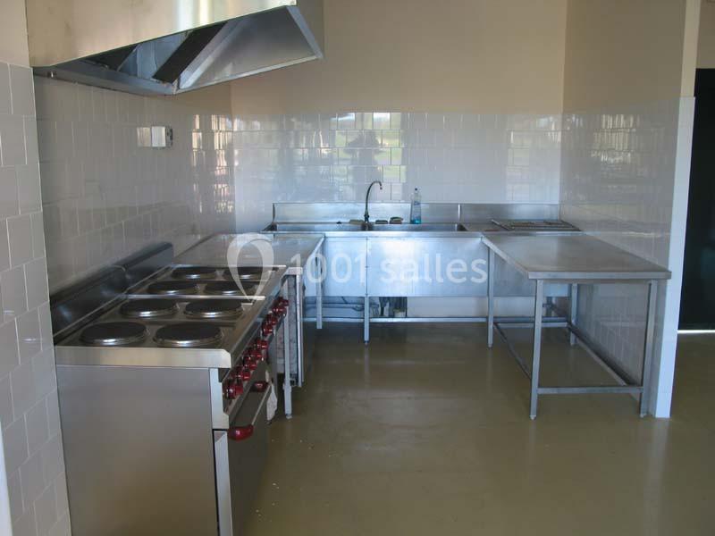 Cuisine professionnelle avec plan de travail en inox, plaques de cuisson, évier et hotte d'extraction.