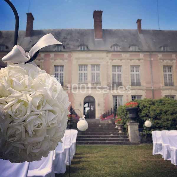 Bouquet de roses blanches suspendu devant une allée décorée, menant à un bâtiment ancien en pierre.