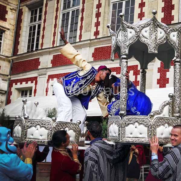 Des artistes en costumes traditionnels sur une plateforme décorée, portée par des personnes lors d'un événement festif.