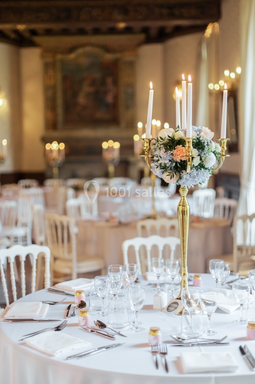 Salle de réception élégante avec tables dressées, chandeliers dorés et décorations florales raffinées.
