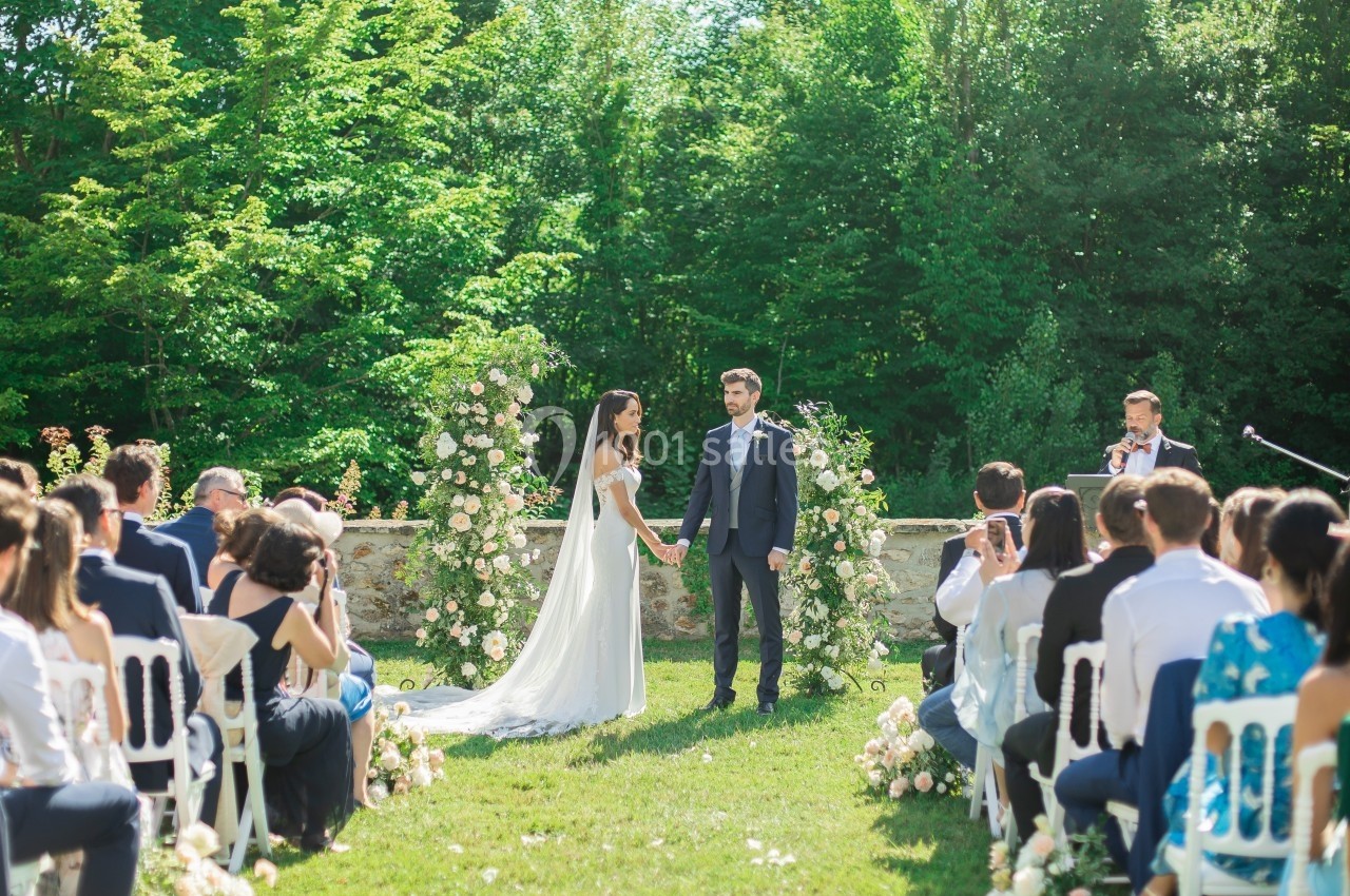 Un couple échange ses vœux lors d'une cérémonie de mariage en plein air, entouré d'invités et de décorations florales.