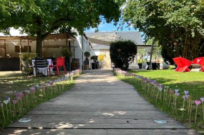 Cabane en bois avec fenêtres et porte vitrées, entourée de fleurs et d'arbustes, située près d'un chemin en gravier.