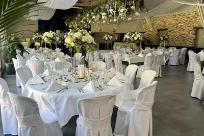 Cabane en bois avec fenêtres et porte vitrées, entourée de fleurs et d'arbustes, située près d'un chemin en gravier.