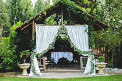 Cabane en bois avec fenêtres et porte vitrées, entourée de fleurs et d'arbustes, située près d'un chemin en gravier.