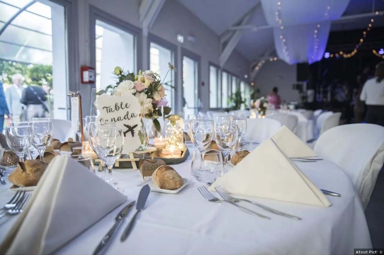 Table décorée pour un mariage avec nappes blanches, serviettes pliées, fleurs, bougies et marque-place ’Table Canada’.