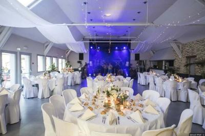 Cabane en bois avec fenêtres et porte vitrées, entourée de fleurs et d'arbustes, située près d'un chemin en gravier.