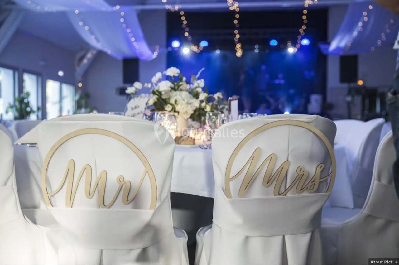 Chaises décorées avec les inscriptions ’Mr’ et ’Mrs’ dans une salle de réception ornée de guirlandes lumineuses.