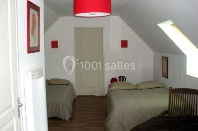 Cabane en bois avec fenêtres et porte vitrées, entourée de fleurs et d'arbustes, située près d'un chemin en gravier.