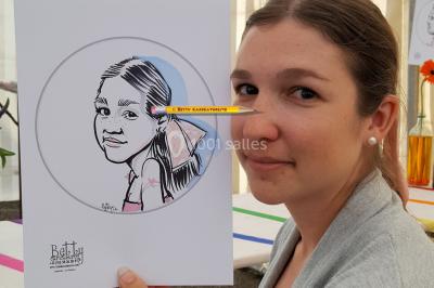 Un homme souriant tient un dessin caricatural de lui-même, réalisé avec des détails humoristiques.