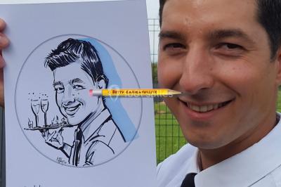 Un homme souriant tient un dessin caricatural de lui-même, réalisé avec des détails humoristiques.