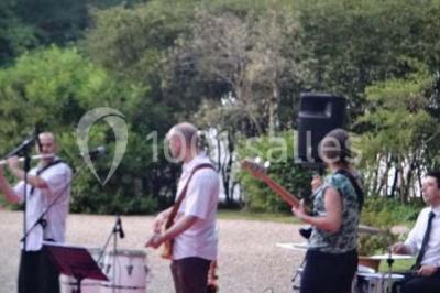 Salle à manger avec table dressée, chaises transparentes, poutre apparente, canapé bleu et tableaux au mur.