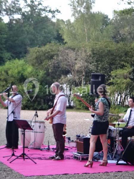 Un groupe de musiciens joue en plein air sur une scène rose, entouré de verdure.