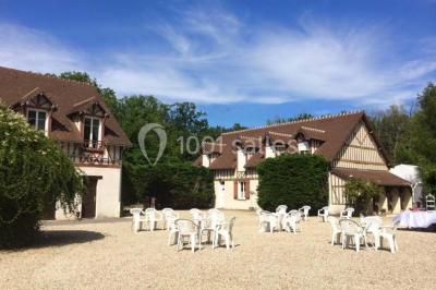 Salle à manger avec table dressée, chaises transparentes, poutre apparente, canapé bleu et tableaux au mur.