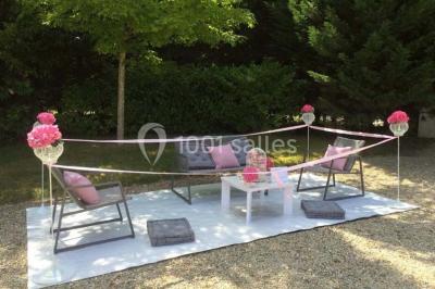 Salle à manger avec table dressée, chaises transparentes, poutre apparente, canapé bleu et tableaux au mur.