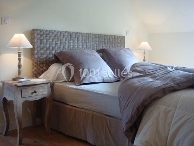 Lit double avec tête de lit en osier, draps beige et oreillers assortis, encadré par deux lampes de chevet allumées.